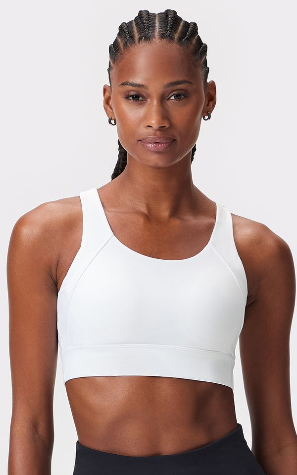 Person with braided hair wearing a white sports bra and hoop earrings, posed against a plain background.