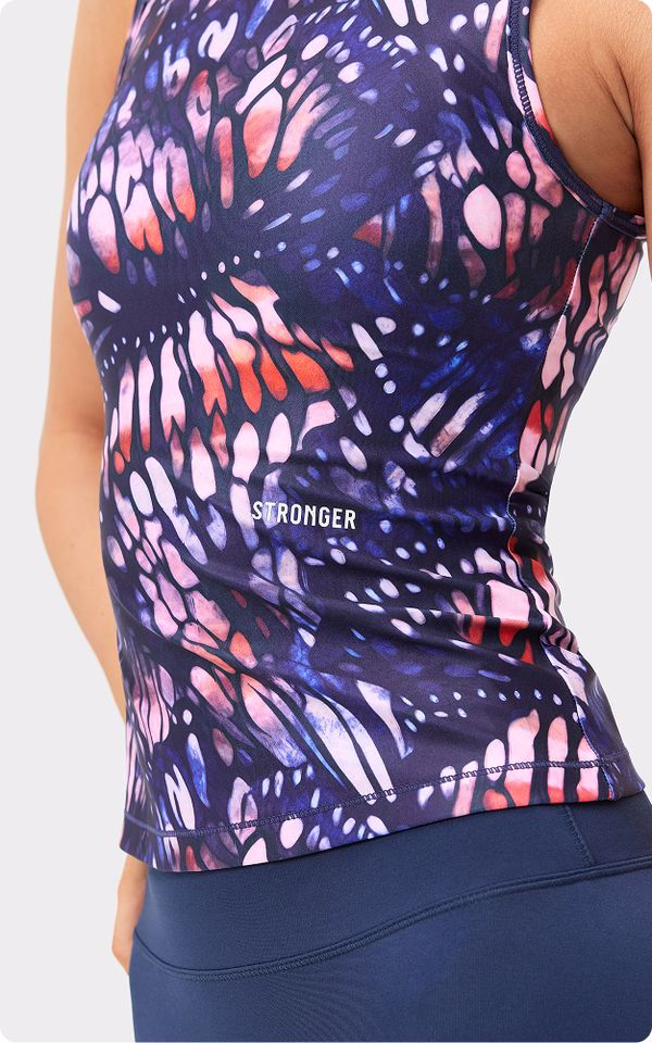 Close-up of a person wearing a colorful, abstract-patterned athletic top with the word "STRONGER" on it, paired with dark blue leggings.