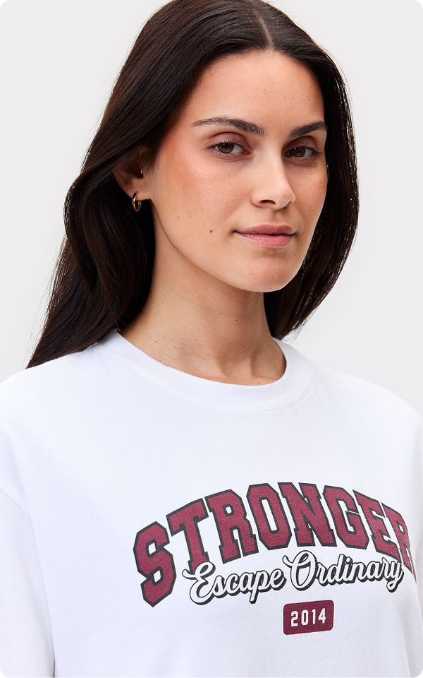 Woman with long dark hair wearing a white shirt with the words "Stronger Escape Ordinary 2014" printed in maroon and black.