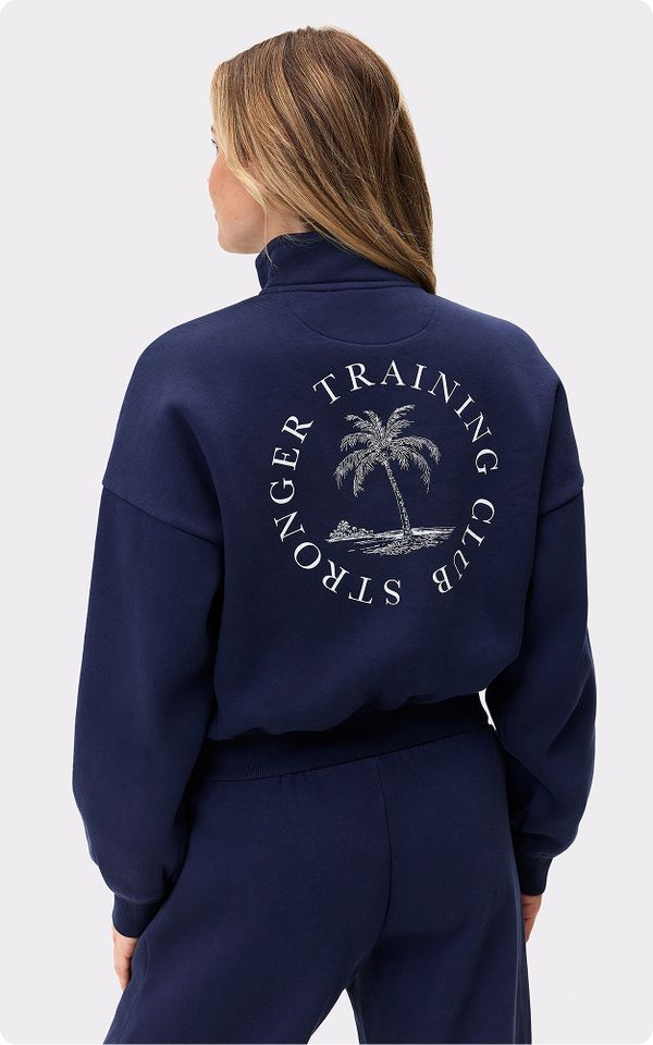 Woman wearing a navy tracksuit with "Stronger Training Club" and a palm tree design on the back, standing with her back to the camera.