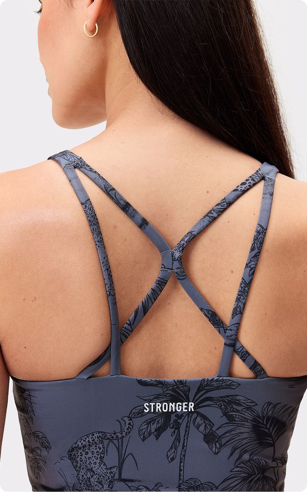 Woman wearing a gray sports bra with a crisscross back design and botanical pattern. The word "STRONGER" is printed on the fabric.