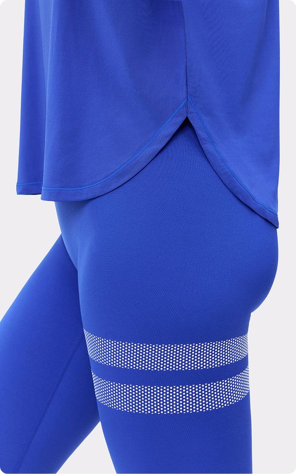 Close-up of a person wearing a bright blue top and leggings with two dotted stripes on the thigh, against a light background.