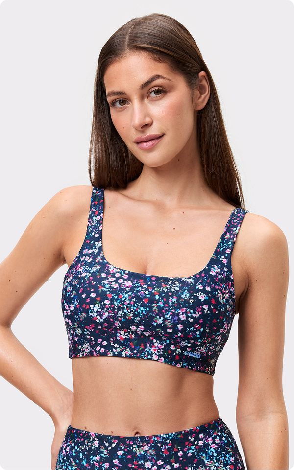 Woman in a navy floral crop top and matching bottoms, with long brown hair, standing against a light gray background.