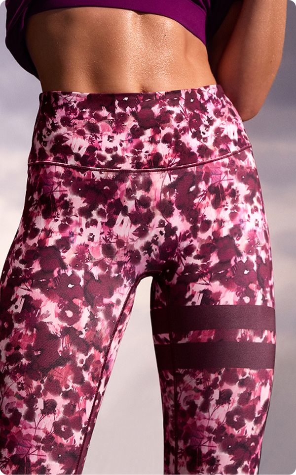 Close-up of a person wearing high-waisted, floral-patterned leggings in shades of pink and red, with a matching crop top.