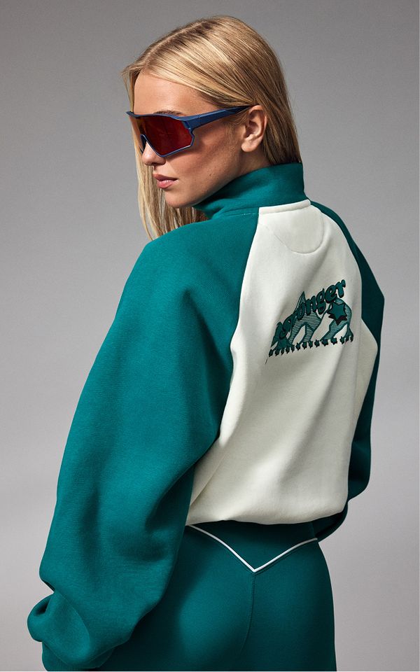 Woman wearing a green and white jacket with logo on the back, paired with matching pants, and oversized sunglasses.