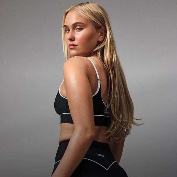 A woman with long blonde hair wearing black activewear, turned slightly to the side, against a neutral background.