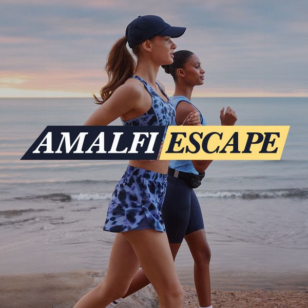 Two women jog on the beach at sunrise, dressed in athletic wear. The text "AMALFI ESCAPE" overlays the image.