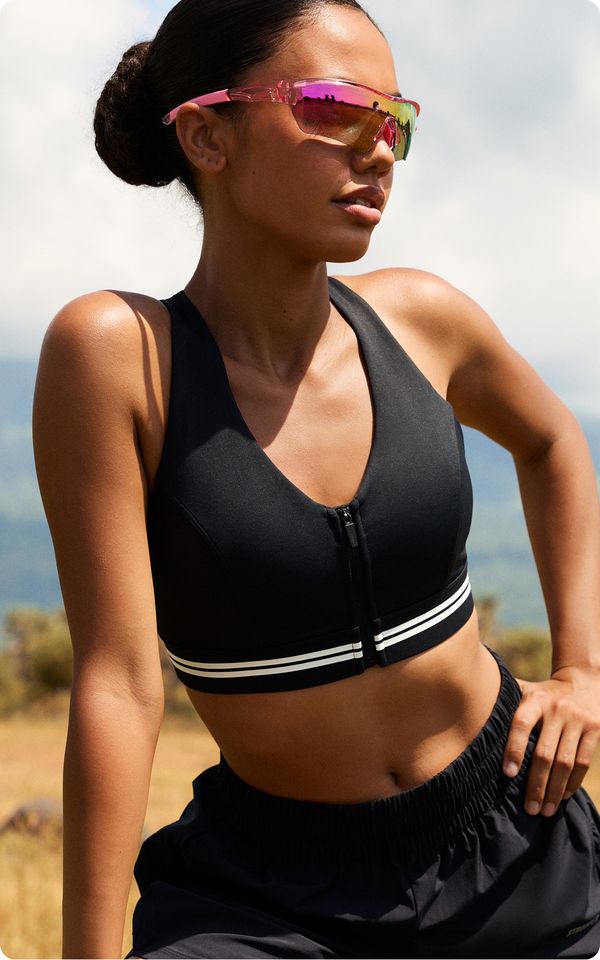 Woman in sporty attire wearing reflective sunglasses, standing outdoors with a scenic background.
