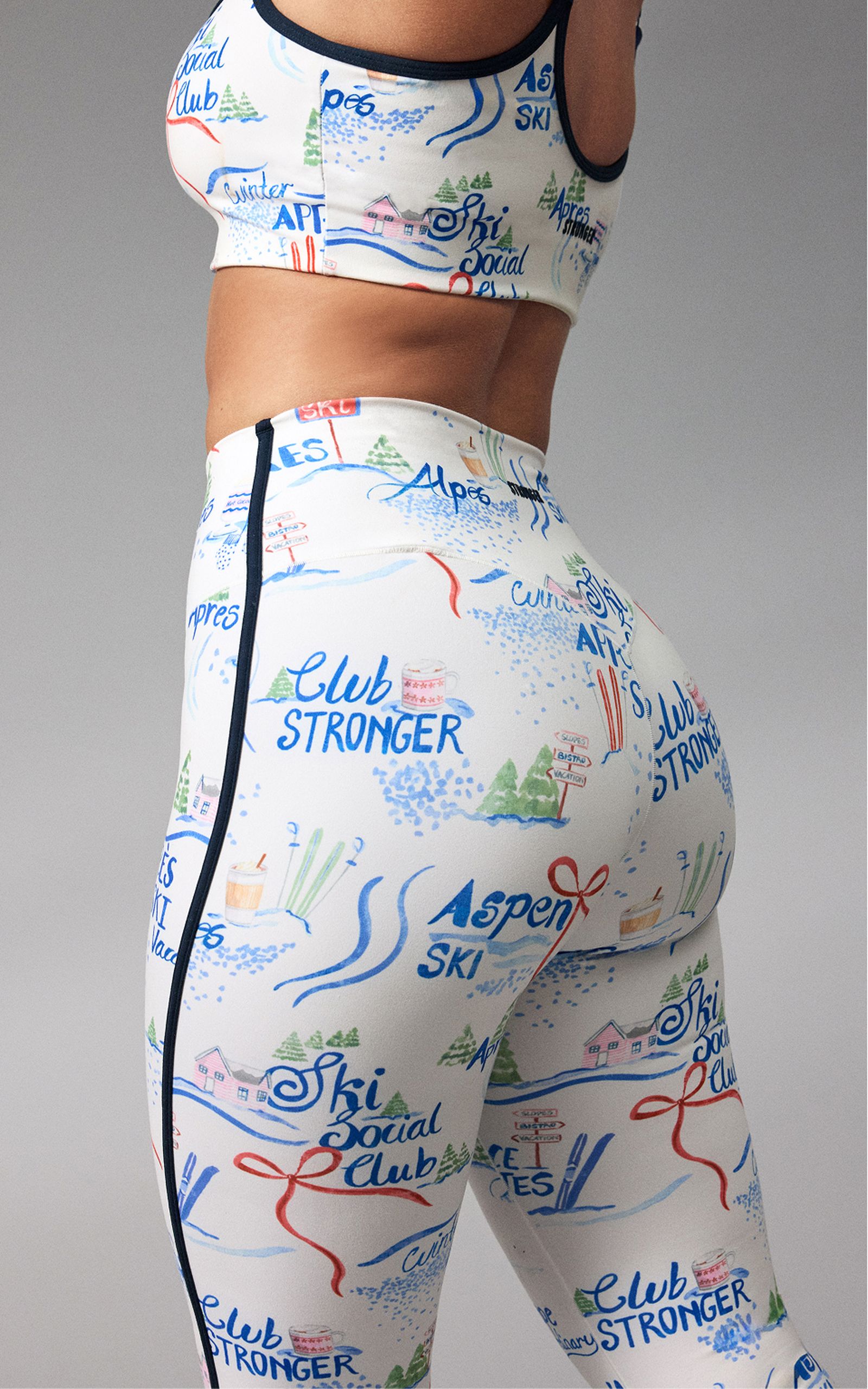 A close-up of a person wearing a sports bra and leggings with colorful ski-themed graphics, including words like "Aspen" and "Ski Social Club."