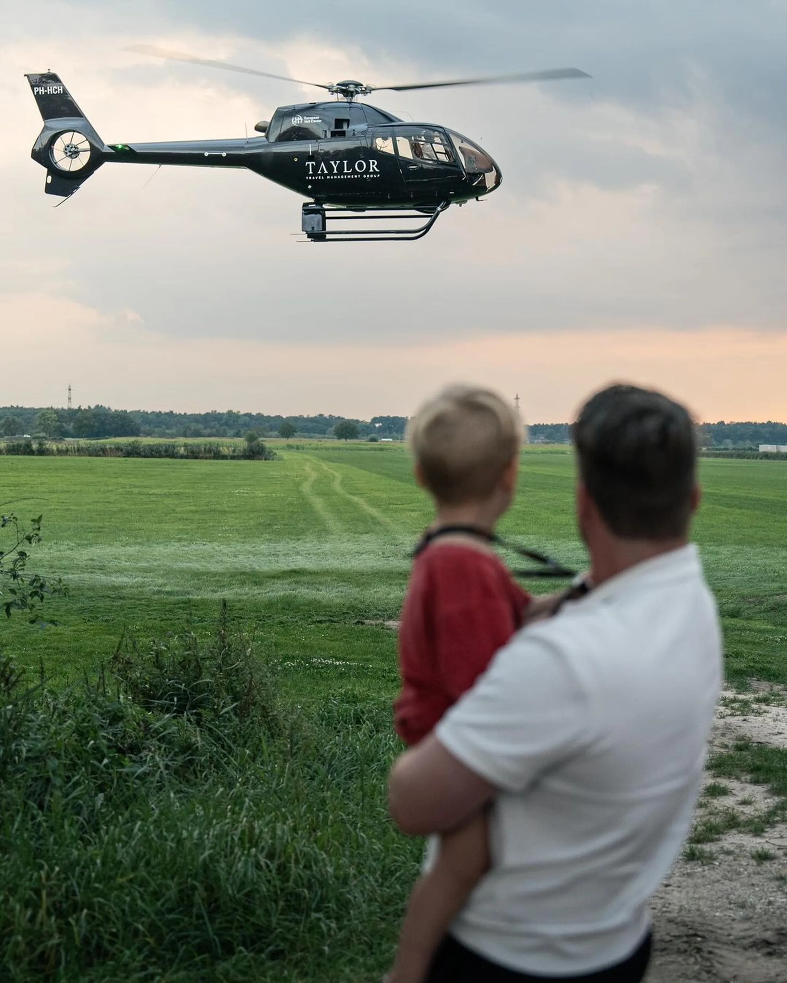 father-and-child-watching-helicopter-flying-over-green-field