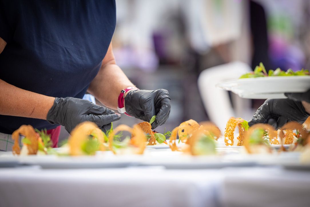 A person wearing black gloves carefully garnishes plates with fresh greens, creating an elegant food presentation.