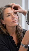 Vrouw bekijkt haar bovenoogleden in een handspiegeltje