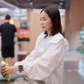 Young Asian woman in a white jacket using a self-checkout kiosk at a retail supermarket, scanning a food item with a smartwatch on her wrist.