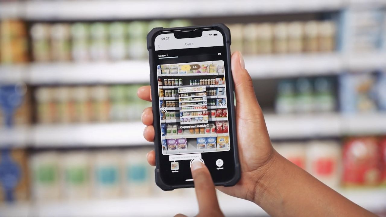 Person using a smartphone to scan grocery shelves, displaying a detailed image of products on the screen.