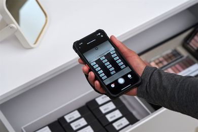 Person holding a smartphone displaying a camera app, aimed at shelves with neatly arranged makeup products in a store.