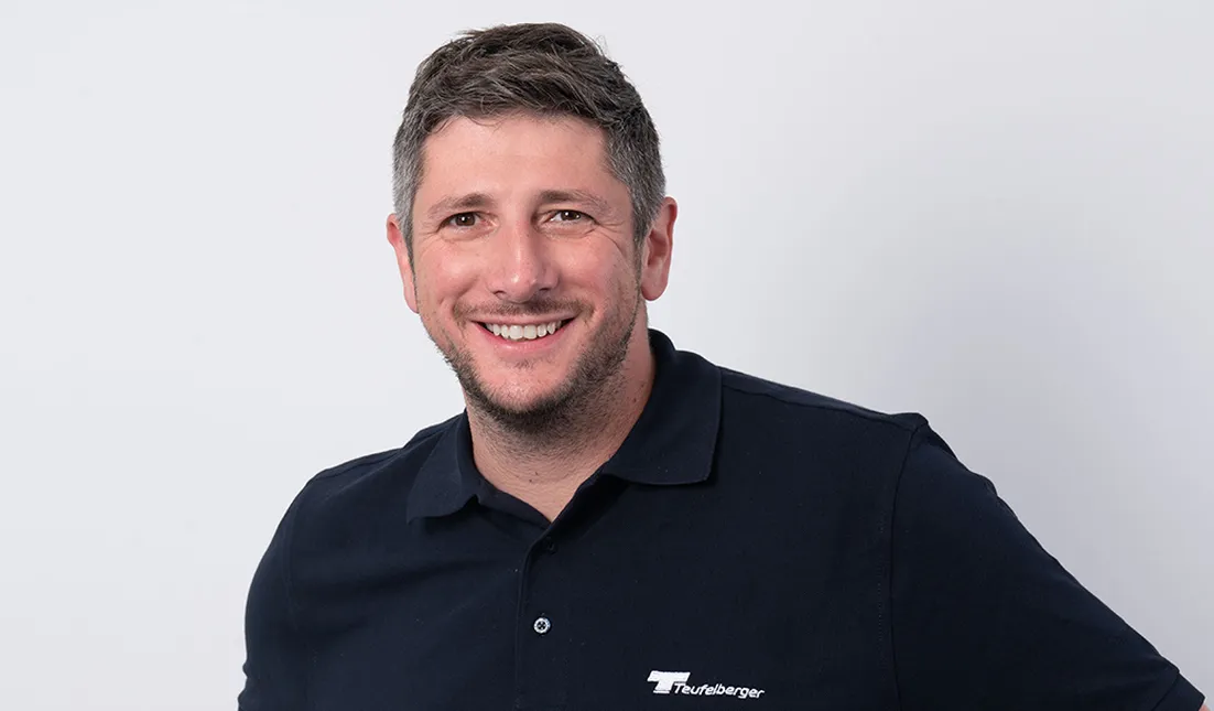 Person wearing a dark-colored polo shirt with “Teufelberger” logo against a plain white background.