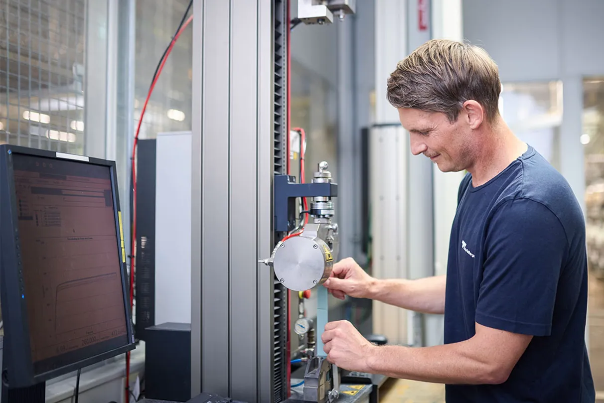 Technician performing tensile strength test on strapping using a testing machine and monitor for data recording