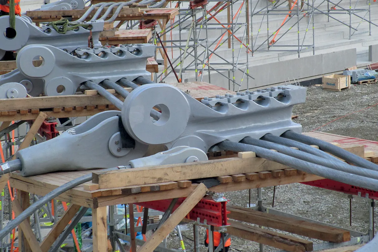 Close-up of large, gray steel bridge components on wooden platforms, surrounded by scaffolding at a construction site.