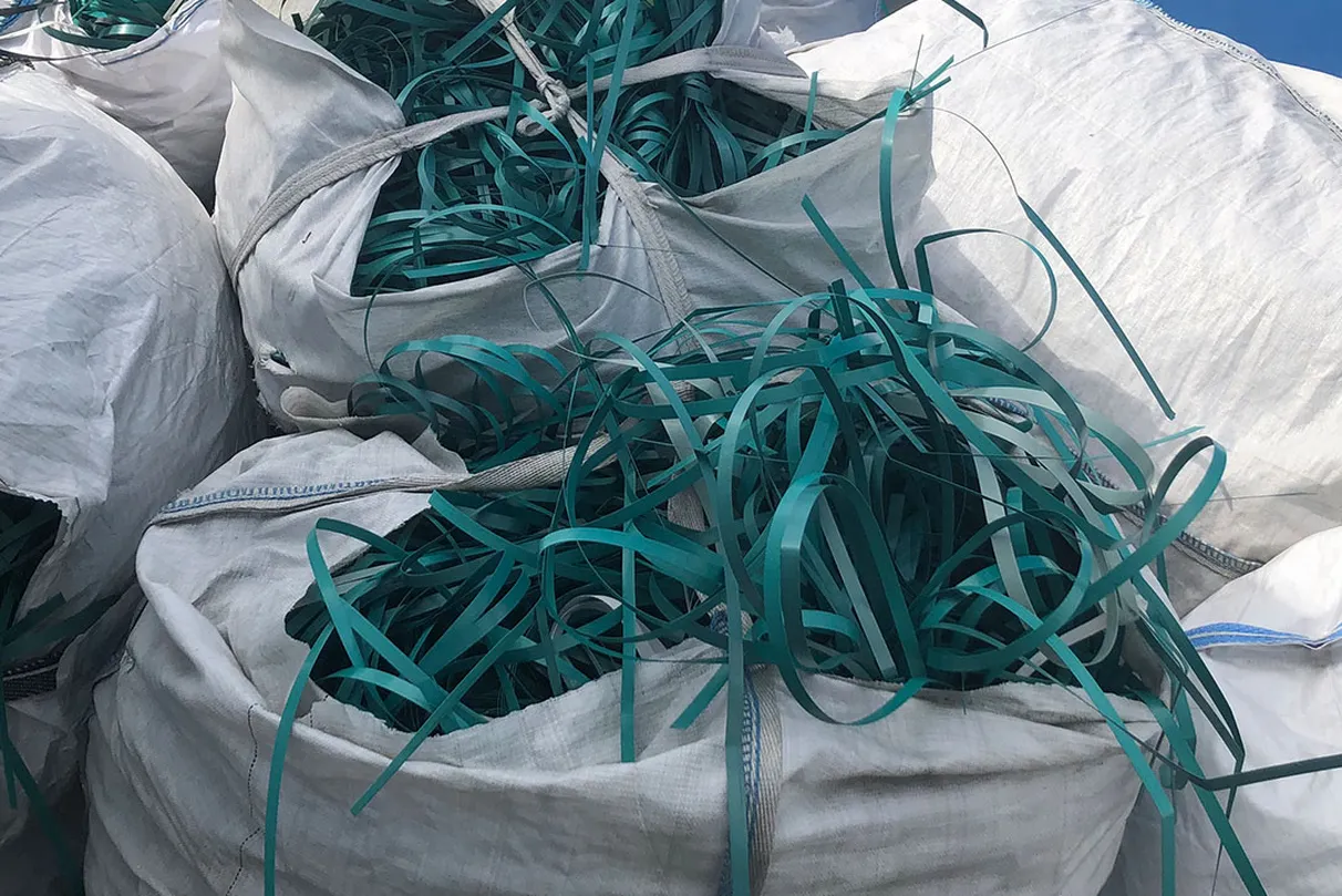 Large white bags filled with long, thin green plastic straps – the strapping spill out from the open tops of the bags.