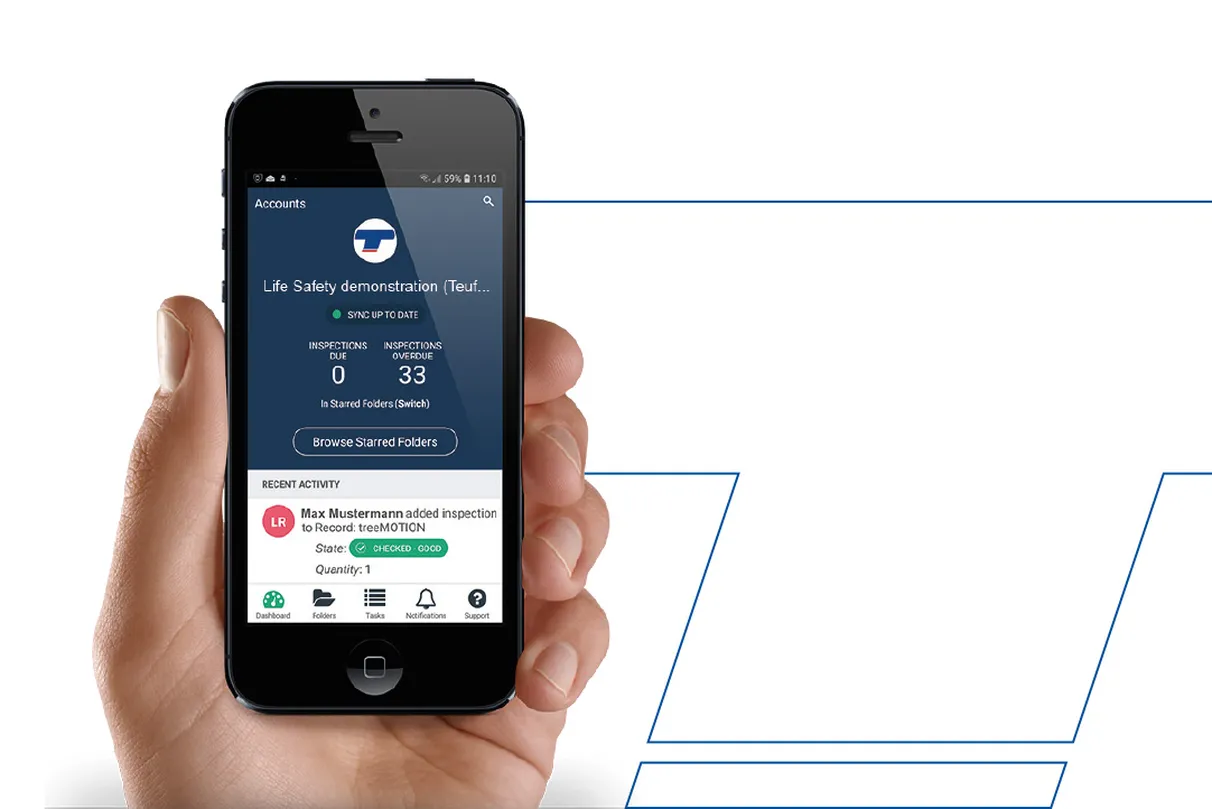 A hand holding a smartphone showing the Life Safety app interface with 33 overdue inspections and a recent activity notification by Max Mustermann.