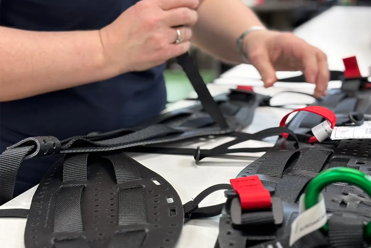 Close up shot of a Teufelberger employee putting together a treeMOTION® harness. She is currently pulling on one of the backstraps while the sitting harness is lying on the table – half way finished.
