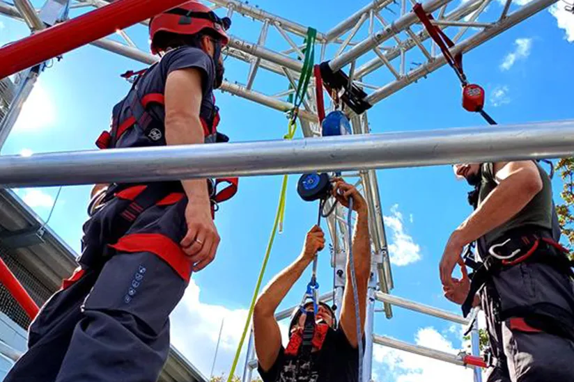Three workers in safety harnesses rigging fiber and wire ropes on scaffolding truss, showcasing quality, innovative rope solutions and safety.