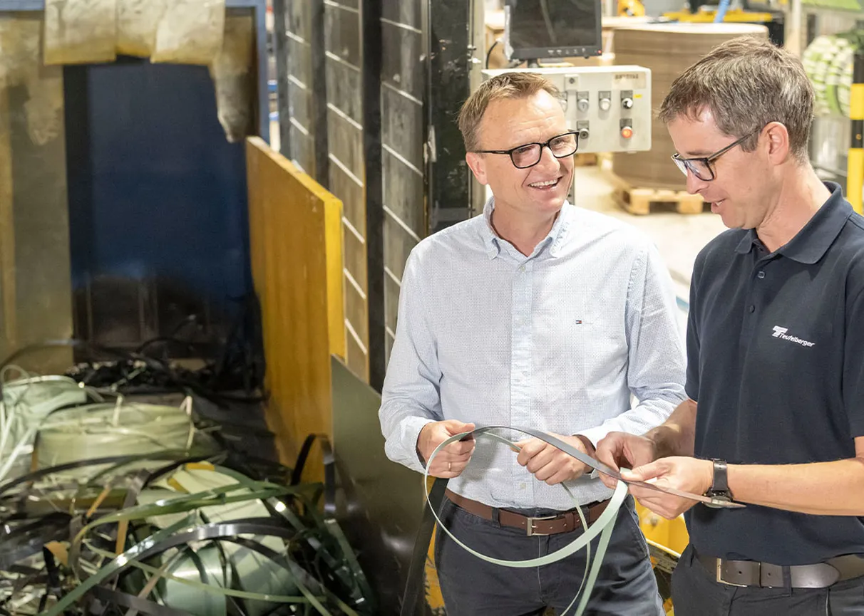better.collect picture showing two men in front of a PET shredder holding used strapping material in hand