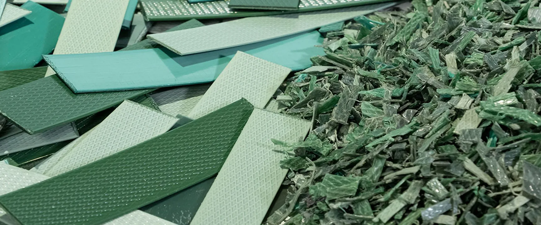 Pile of green and light green plastic pieces – some flat and textured, others shredded – representing recycled material.
