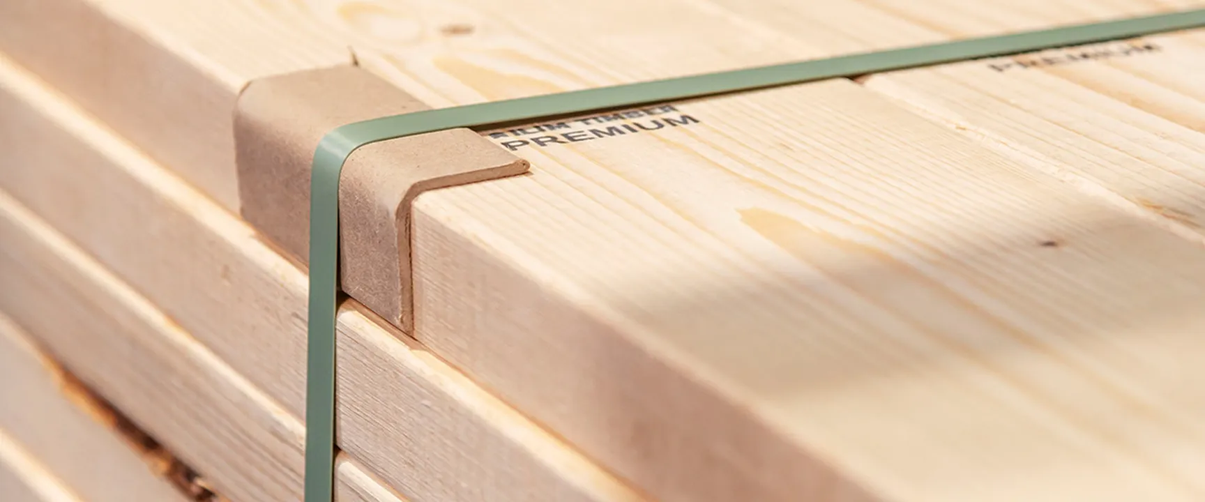 Stacked premium wooden planks secured with cardboard edge protectors and a green strap – high-quality packaging and labeling of top-grade lumber for construction and trade.