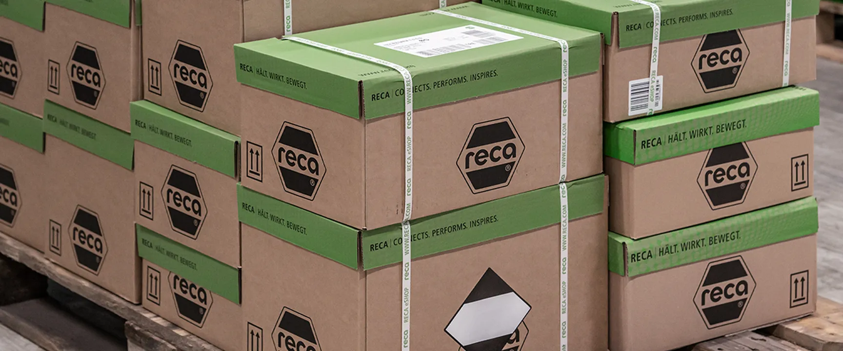 Stacked RECA boxes on a wooden pallet with green accents and safety markings – efficient, brand-focused packaging solution for logistics and secure goods transportation.