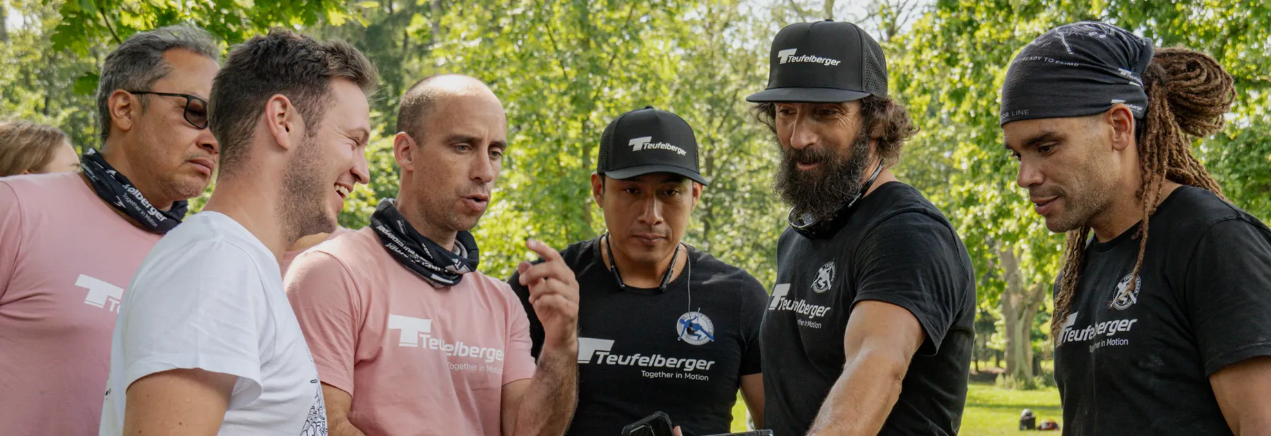 Group of Teufelberger Ambassadors in brand tshirts standing together and looking on a picture one of them is showing them on the phone.