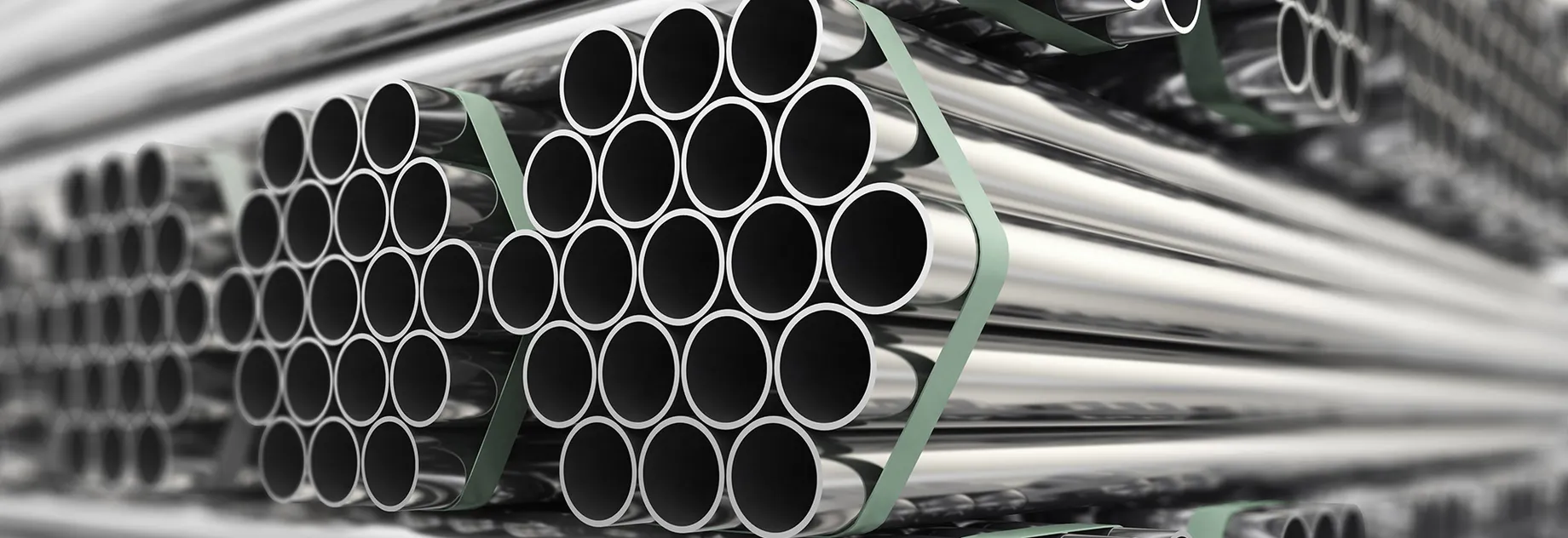 Close-up of several bundles of shiny metal pipes, neatly stacked and secured with green strapping; focus on the open pipe ends.