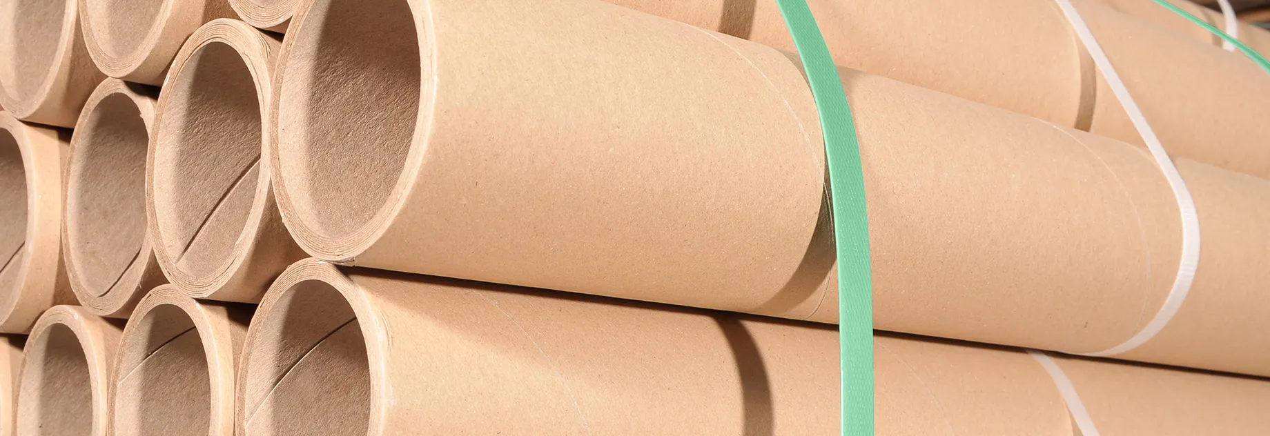 Stack of corrugated cardboard sheets, neatly piled and secured with a white strapping band; the corrugated structure is clearly visible from the side.