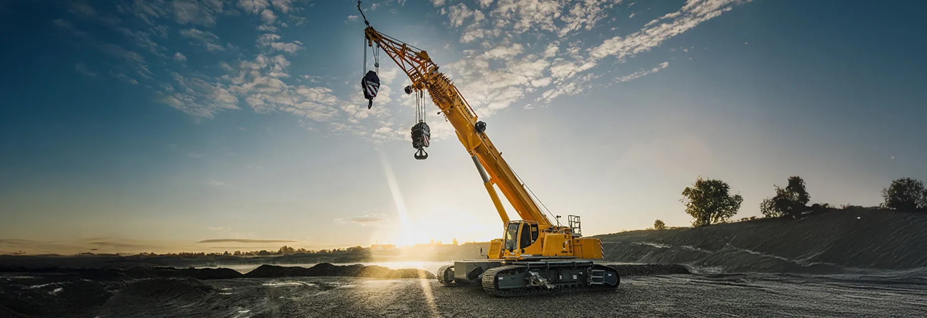 Großer gelber Raupenkran auf einer Baustelle bei Sonnenaufgang, symbolisiert Stärke und Effizienz in der Bauindustrie.