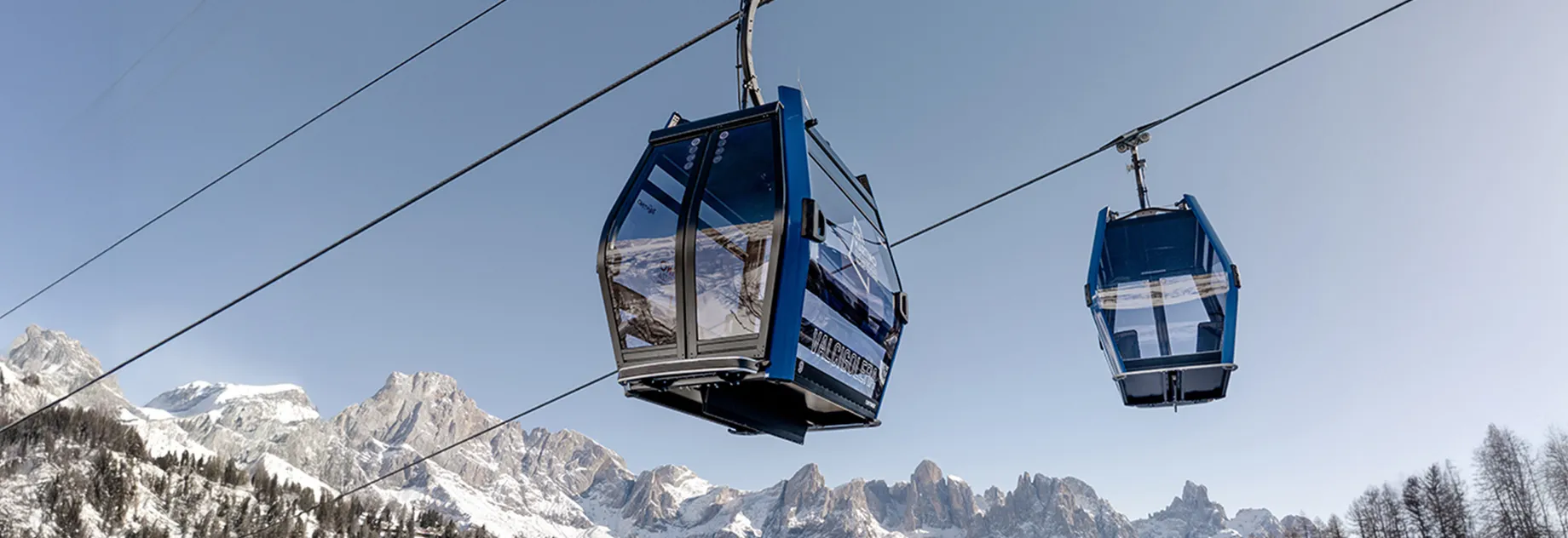 Two blue gondola cabins suspended on cables in a snowy alpine landscape – representing safe and compliant cable car operation through expert inspection and maintenance