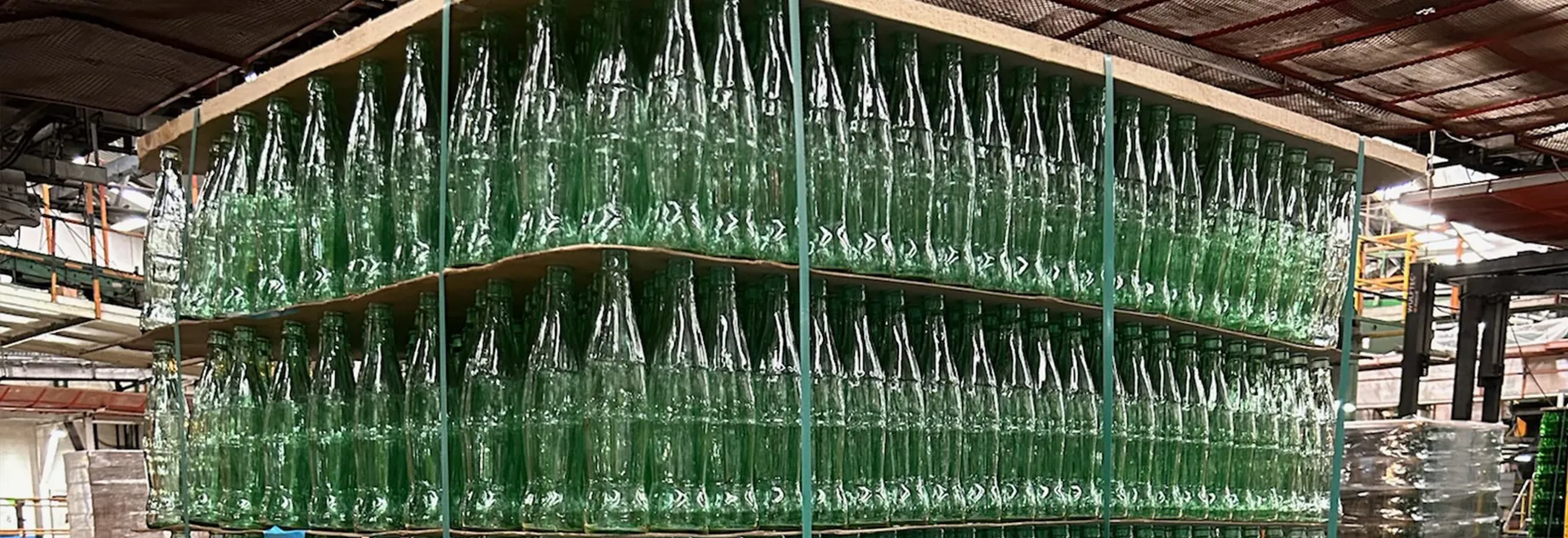 Large stack of empty glass bottles with yellow labels, arranged in multiple rows and columns on a pallet.