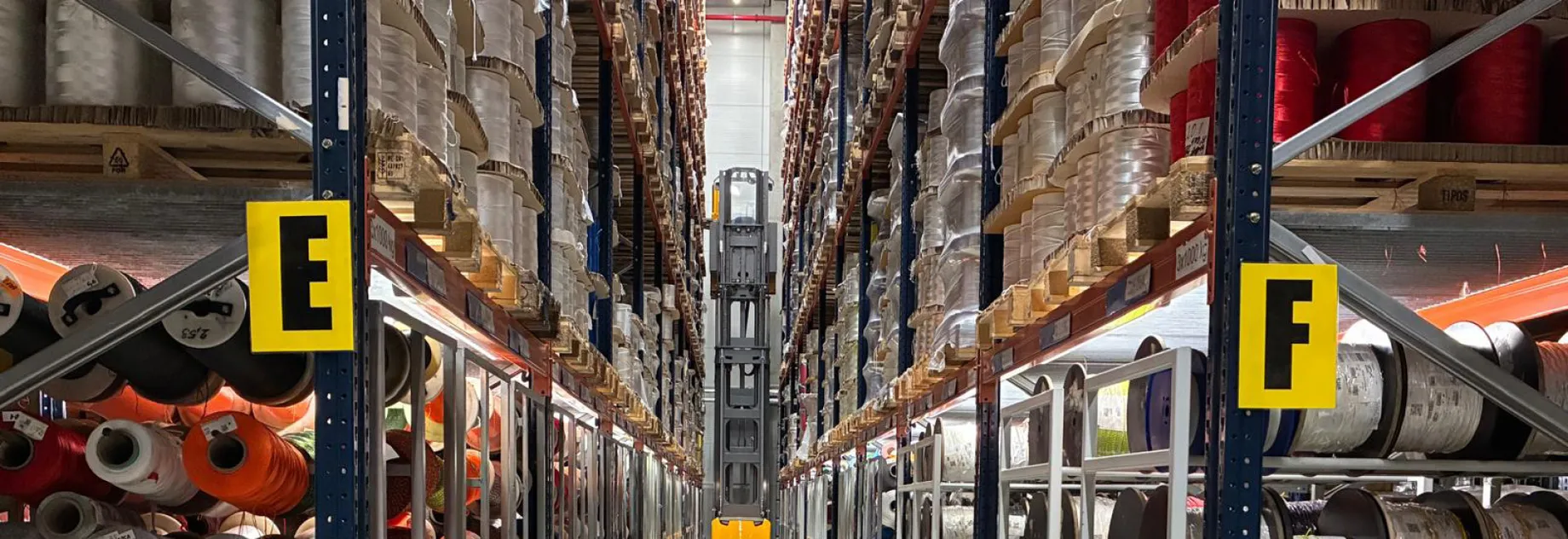 A warehouse aisle filled with shelves of fiber ropes and materials, with a forklift in the center.