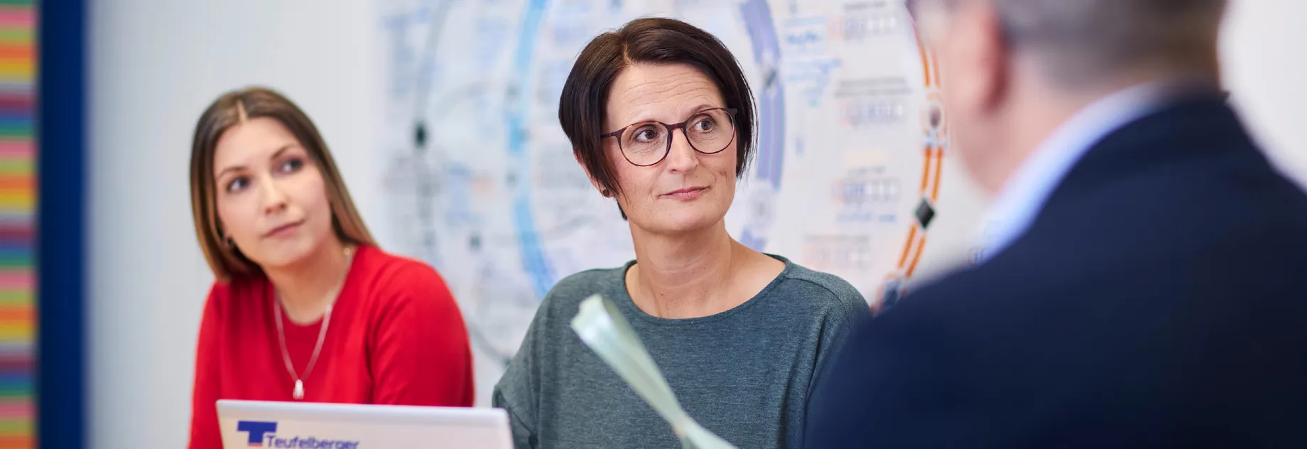 People discussing during a meeting with a laptop and a diagram in the background for strategic planning