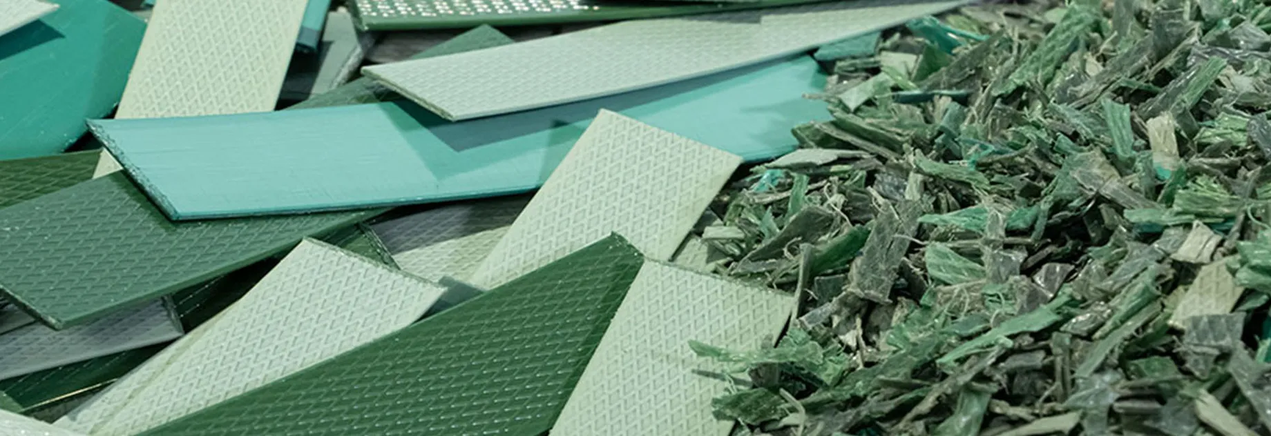 Pile of green and light green plastic pieces – some flat and textured, others shredded – representing recycled material.