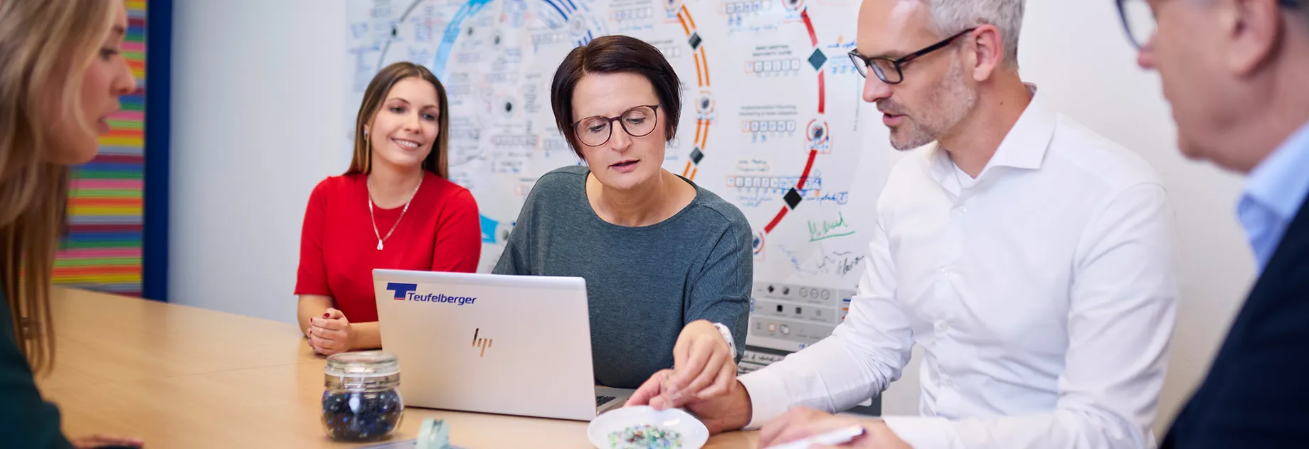 Team discussing plastic granules and circular economy concepts, with a laptop and process diagram in the background