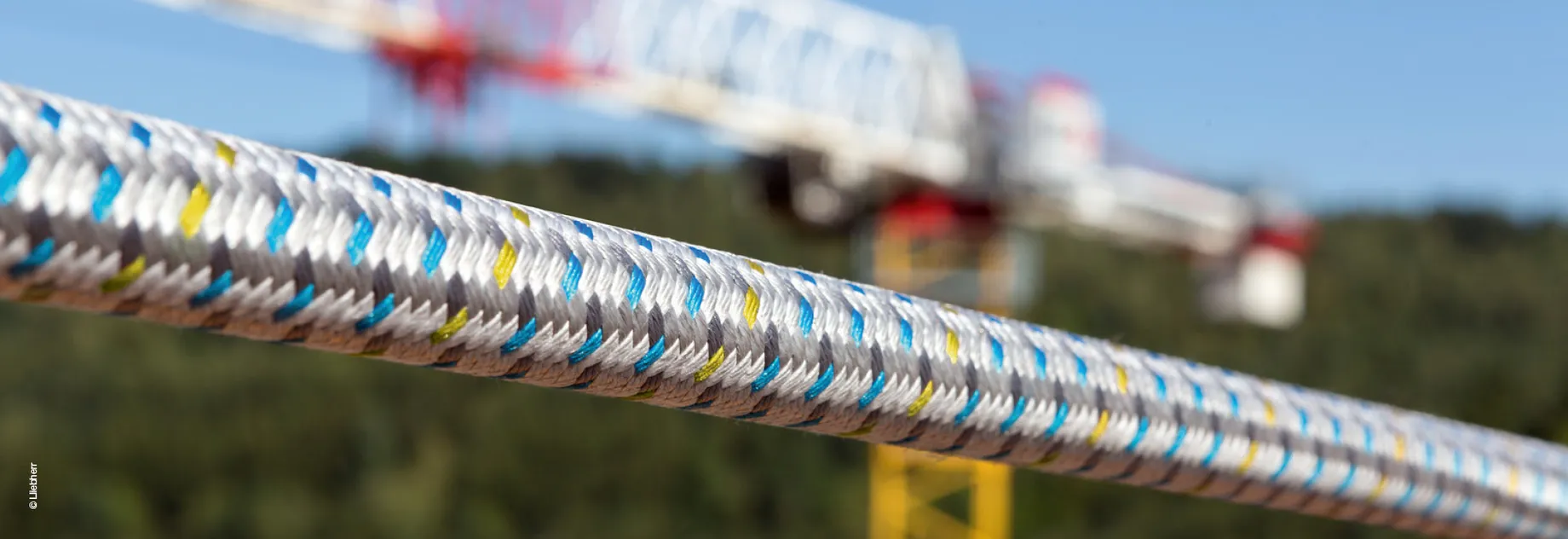 Close-up of a durable, multi-colored fiber rope with a blurred construction crane in the background.