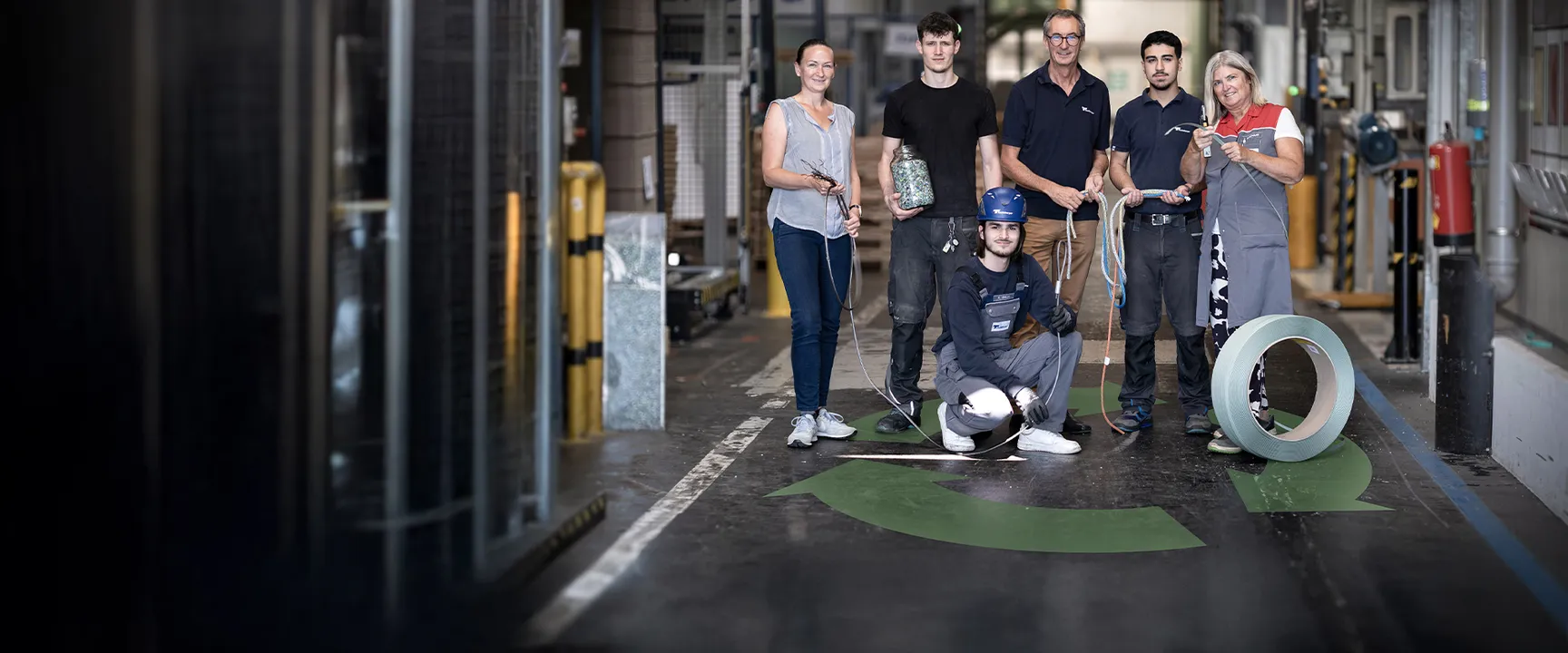 A team of six factory workers in a warehouse, standing and crouching with various tools and materials, showcasing teamwork and professionalism.