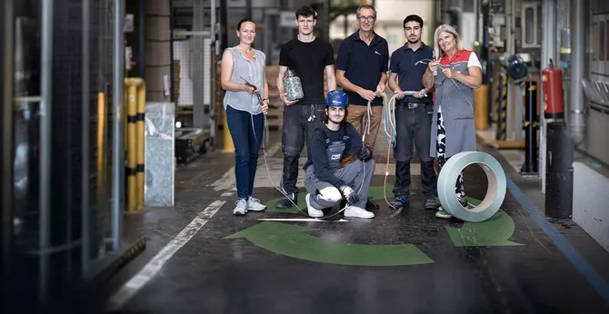 A team of six factory workers in a warehouse, standing and crouching with various tools and materials, showcasing teamwork and professionalism.