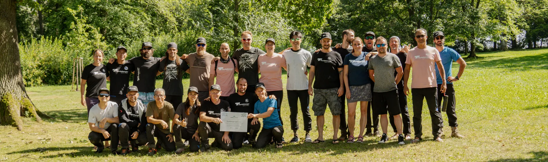 Group of people in a park with trees and grass, some holding a sign – symbolizing community, engagement, and sustainability in a green environment.