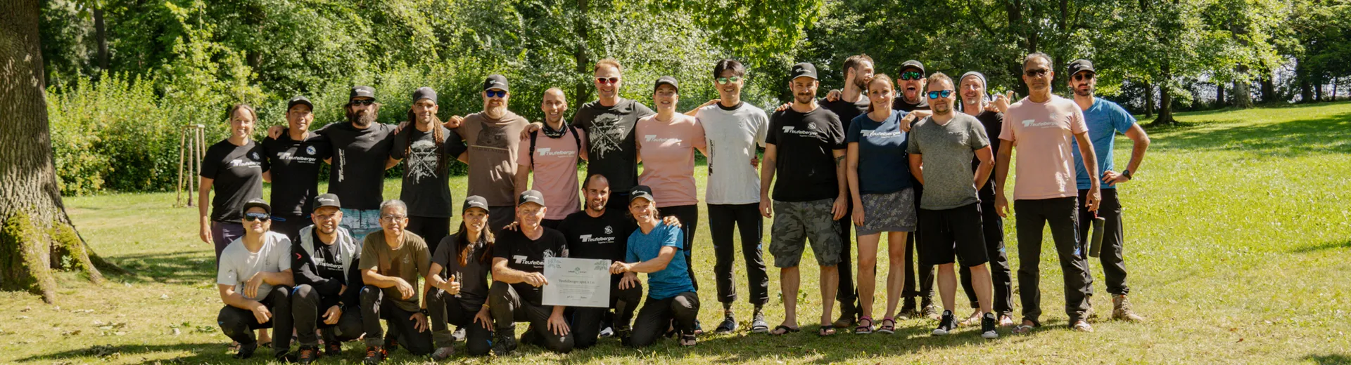Group of people in a park with trees and grass, some holding a sign – symbolizing community, engagement, and sustainability in a green environment.