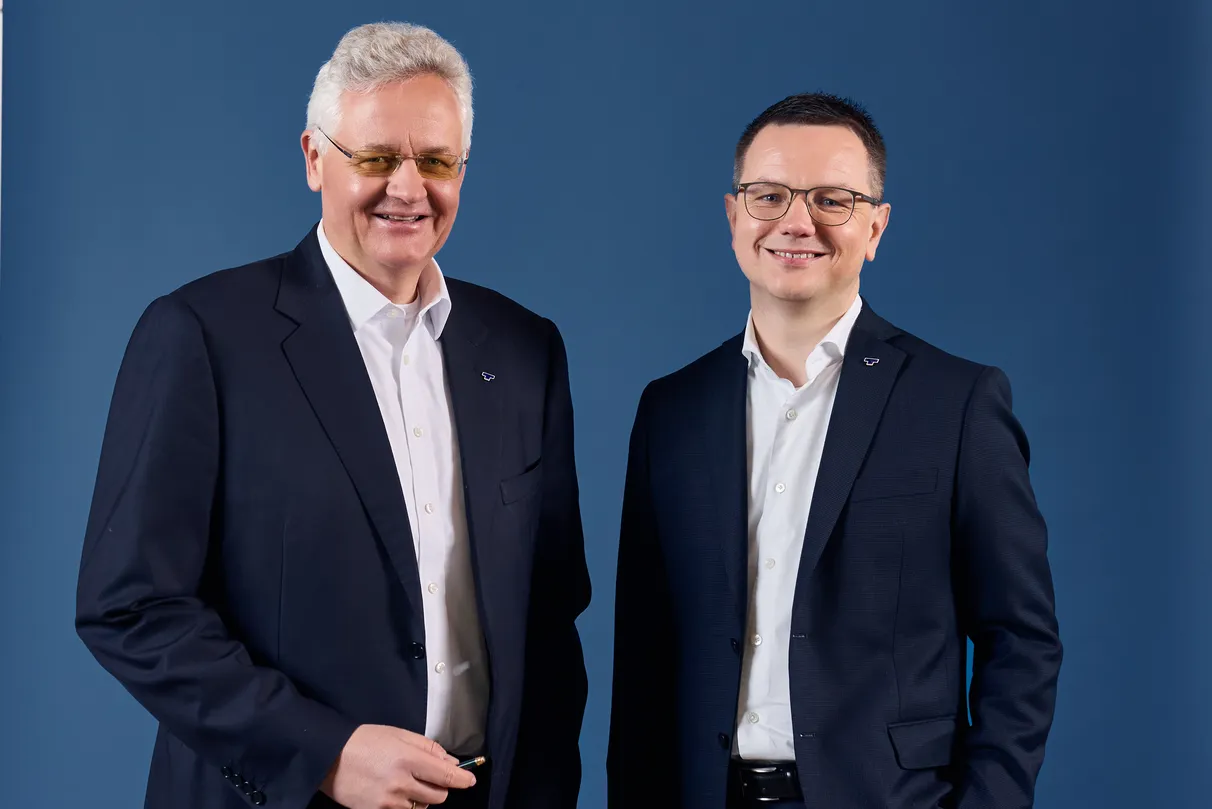 Two men in suits smiling against a blue background.