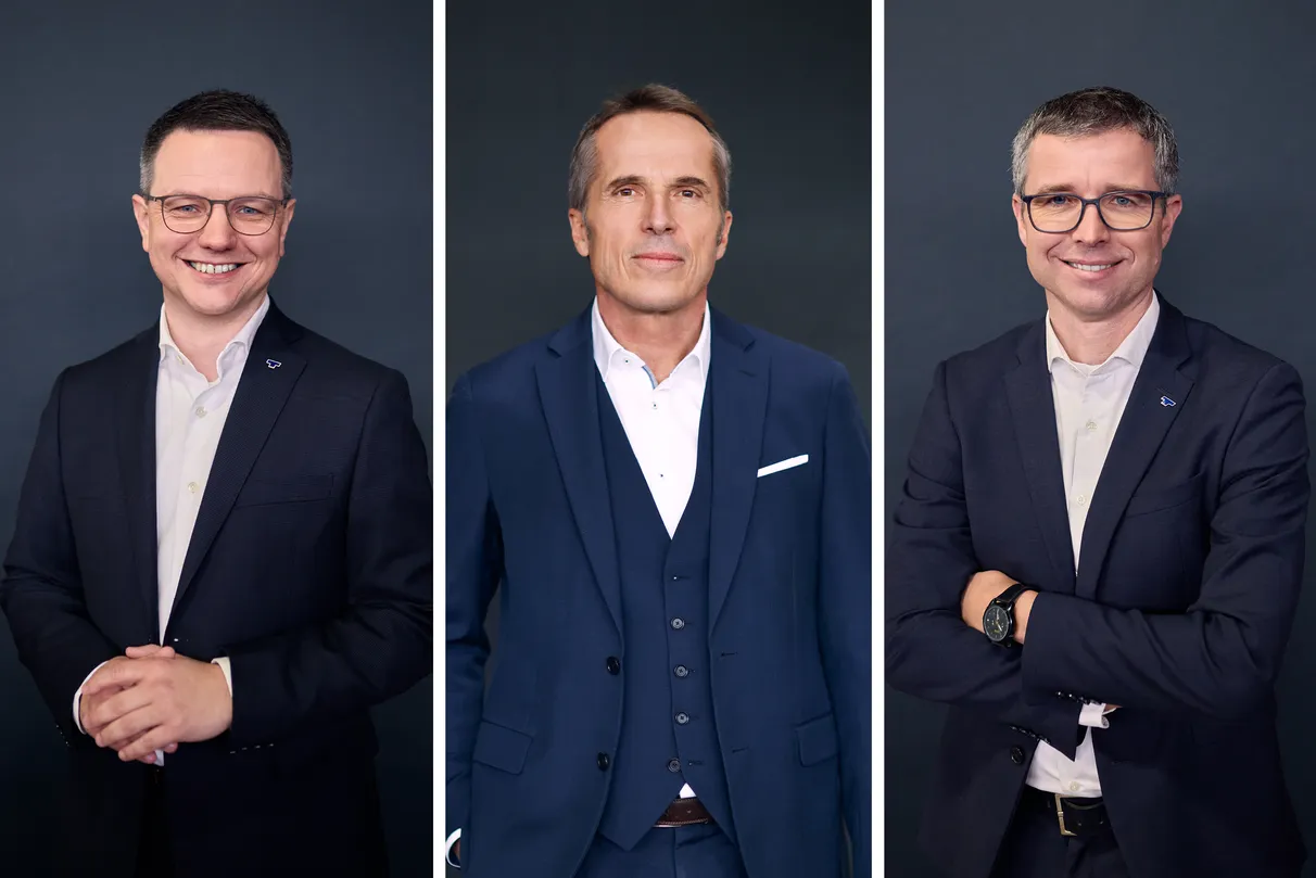 Three men in business attire, each wearing a suit and smiling confidently against a neutral background.