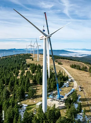 Wind turbine construction on a hilltop with crane support – sustainable energy generation in a mountainous landscape.