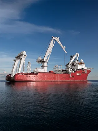 Large red vessel with cranes and equipment on calm water under a clear sky – maritime technology for heavy-duty and offshore operations.