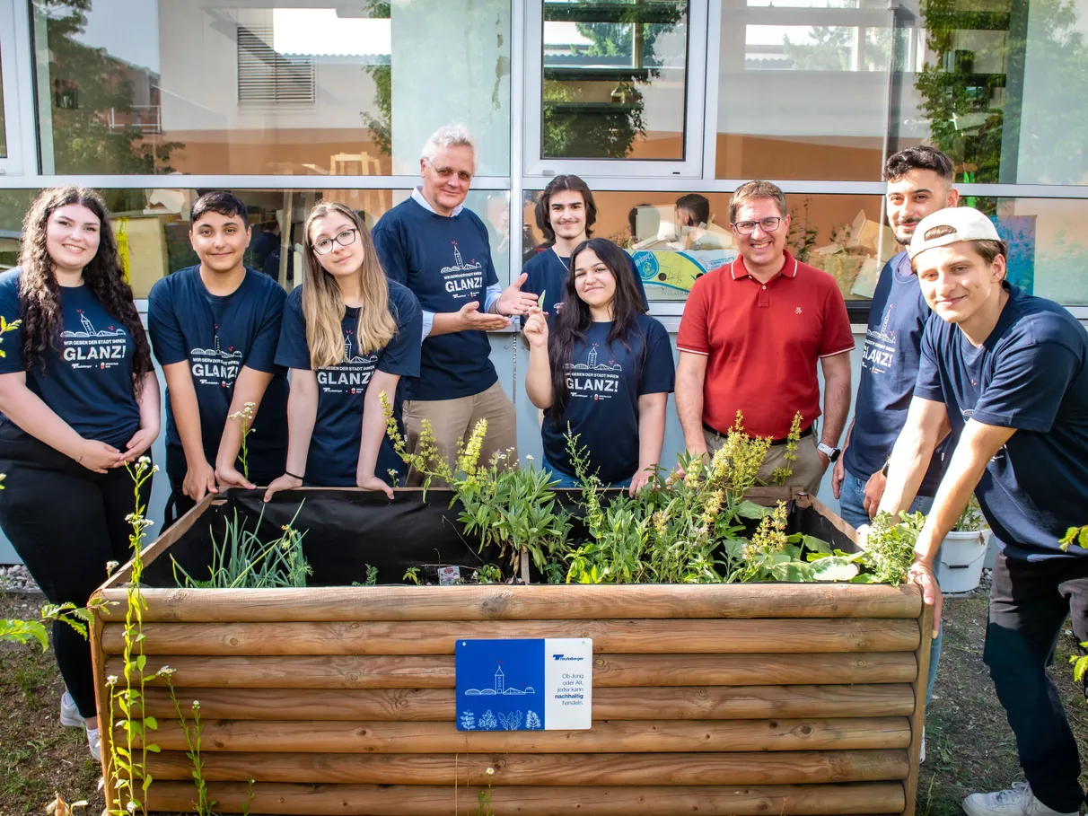 A group of young people is visible behind a raised garden bed with plants.